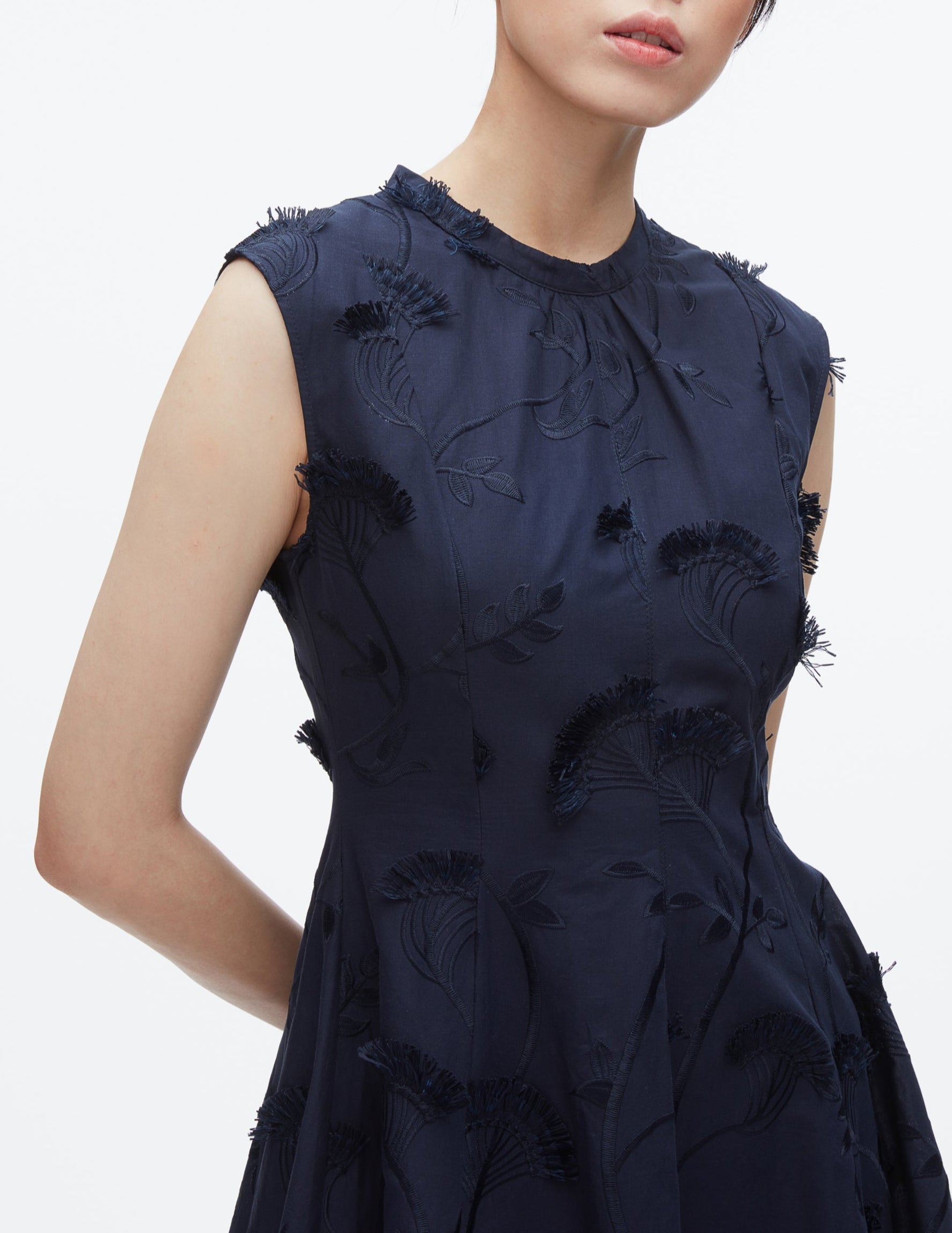 A woman stands against a plain white background wearing the 3.1 Phillip Lim Fil Coupé Midi Dress—a sleeveless, dark blue cotton voile dress with textured floral embroidery.