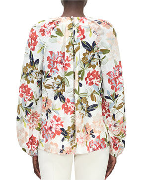 A person is seen from the back wearing the Adam Lippes Lottie Top, a long-sleeve white crepe de chine blouse with an ivory floral motif, paired with white pants.