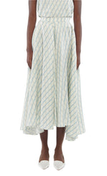 A person wears the Sloan Silk Twill Skirt by Adam Lippes—a light blue and white checkered silk skirt with an uneven hem—paired with white pointed-toe shoes, shown from shoulders to feet.