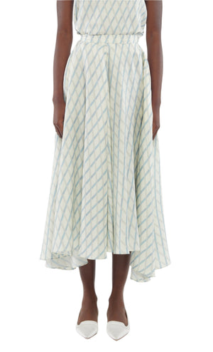 A person wears the Sloan Silk Twill Skirt by Adam Lippes—a light blue and white checkered silk skirt with an uneven hem—paired with white pointed-toe shoes, shown from shoulders to feet.