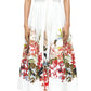 A woman wears the Adam Lippes Attacher Dress, a white collared short-sleeve midi dress with a waist sash and colorful floral print on the skirt, paired with white sandals.