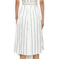 A woman shown from the back wears the Adam Lippes Nansi Stripe Dress—a white knee-length poplin dress with vertical black stripes, short sleeves, a belted waist, and an asymmetrical hem—paired with black strappy heels.