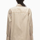 Person with braided hair wears the 3.1 Phillip Lim Asymmetrical Stripe Trapeze Shirt, featuring beige and white stripes and oversized cuffs, viewed from the back against a plain white background to showcase its relaxed silhouette.