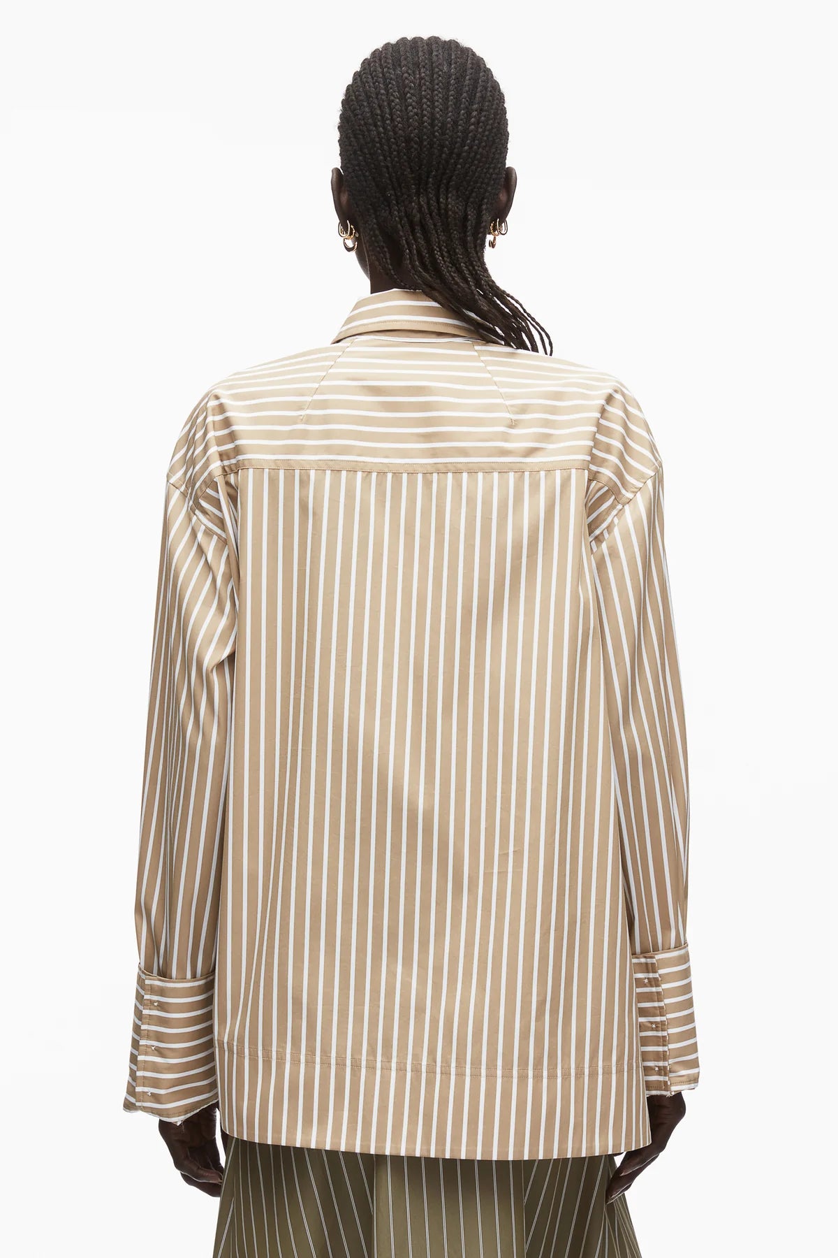 Person with braided hair wears the 3.1 Phillip Lim Asymmetrical Stripe Trapeze Shirt, featuring beige and white stripes and oversized cuffs, viewed from the back against a plain white background to showcase its relaxed silhouette.
