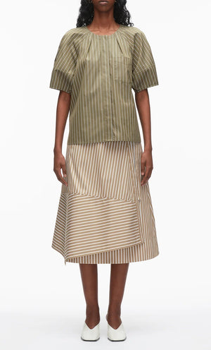 A woman wears the 3.1 Phillip Lim Stripe Lantern Sleeve Shirt in olive green with a beige striped midi skirt featuring asymmetrical layers and an A-line silhouette, paired with white shoes.