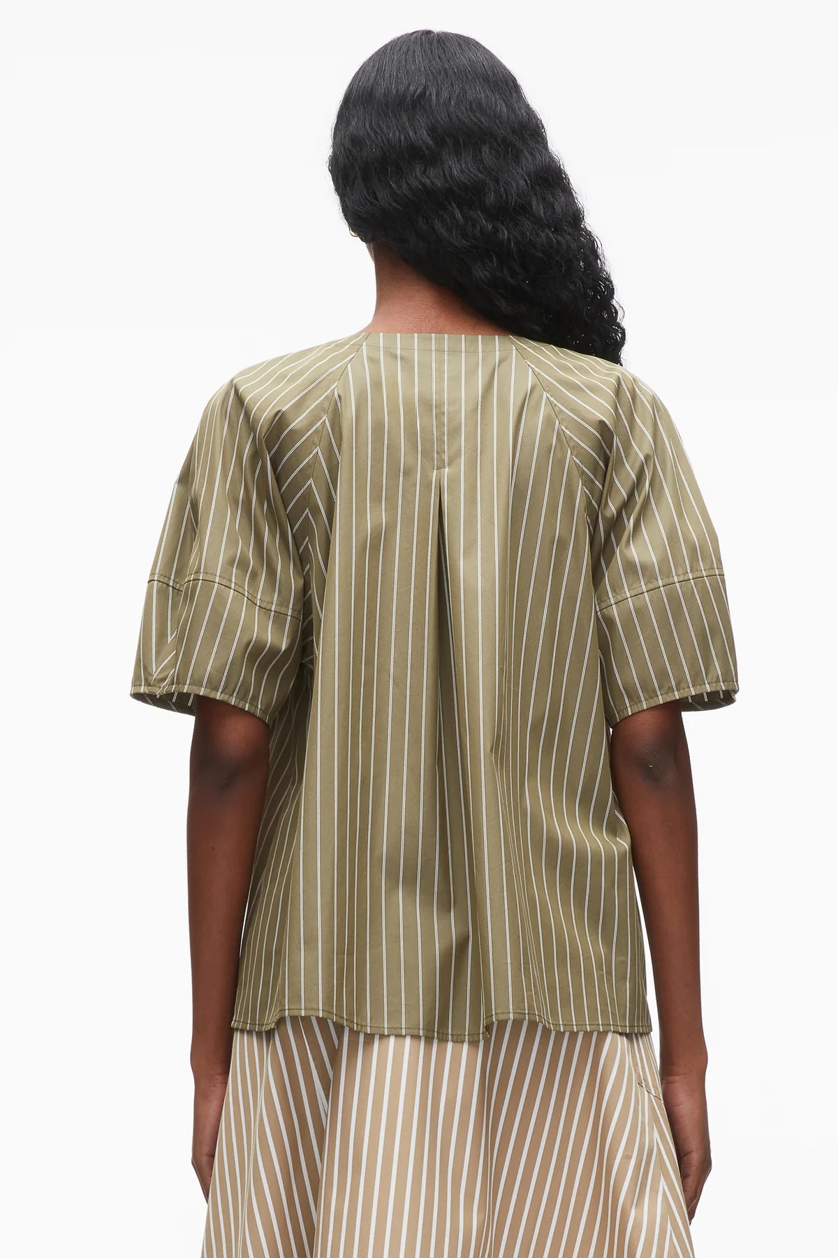 A person stands facing away, wearing the 3.1 Phillip Lim Stripe Lantern Sleeve Shirt with vertical white stripes and sculptural sleeves, paired with a matching skirt.