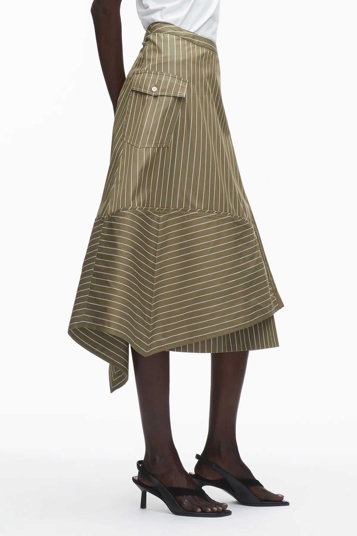 A person models the 3.1 Phillip Lim Stripe Wrap Asymmetrical Hem Skirt with a handkerchief hem and large side pocket, paired with black heeled sandals, set against a white background.
