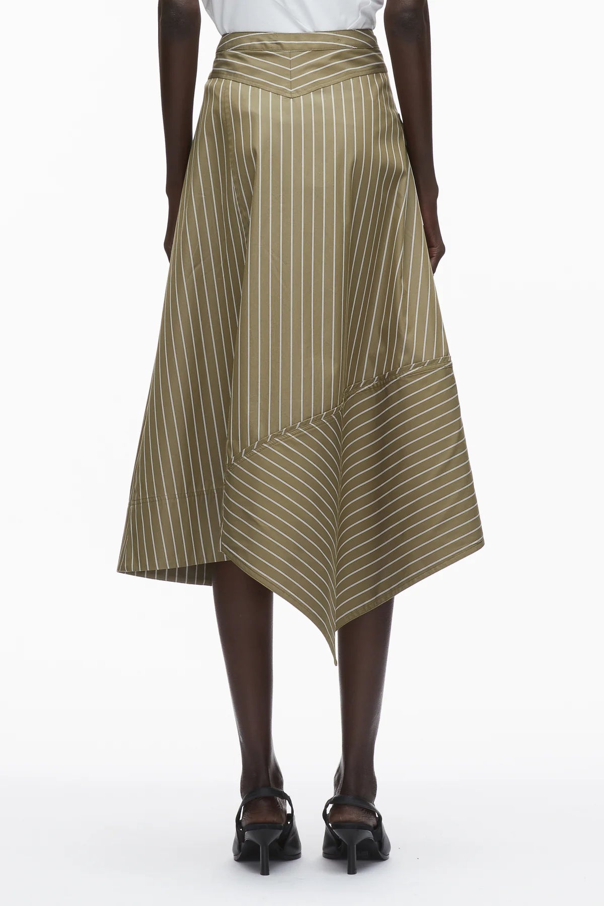 A person in the 3.1 Phillip Lim Stripe Wrap Asymmetrical Hem Skirt, featuring khaki cotton with white vertical and diagonal pinstripes, styled with black heeled sandals.
