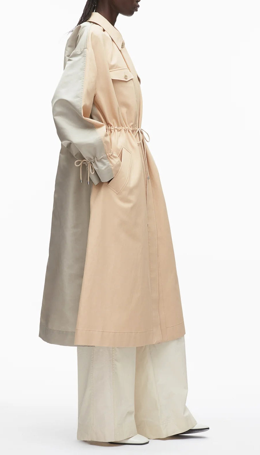 A person in profile wears the 3.1 Phillip Lim Blouson Trench Coat—a long, modern two-tone cotton-viscose twill coat with a drawstring waist—over wide-leg pants, standing against a plain background.