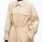 A person wearing the 3.1 Phillip Lim Blouson Trench Coat, a beige cotton-viscose utility jacket featuring buttoned chest pockets, side pockets, drawstring waist, and contrasting light sleeve panels for a modern touch.