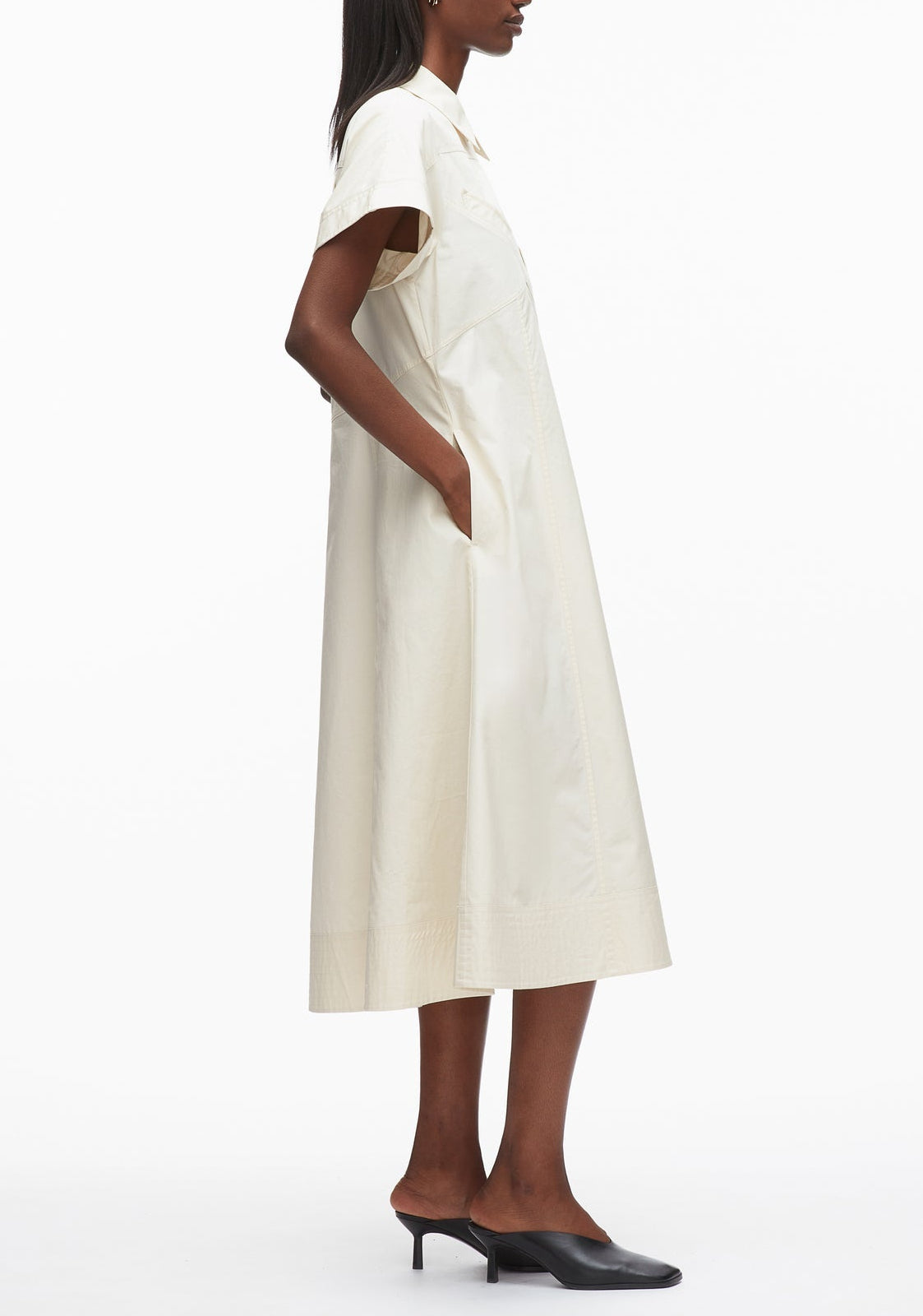 A person stands in profile wearing the 3.1 Phillip Lim Trapeze Midi Poplin Shirt Dress with side pockets and black heeled mules against a plain white background.