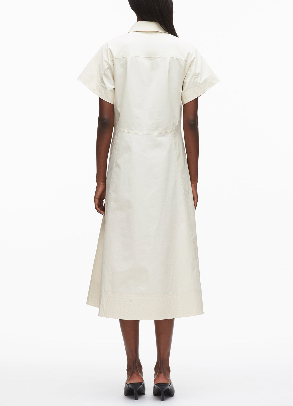A person stands facing away, wearing the 3.1 Phillip Lim Trapeze Midi Poplin Shirt Dress in off-white with black heels against a plain white background.