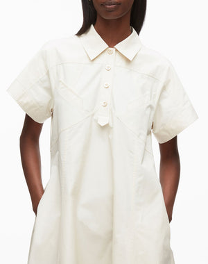 A person wears the 3.1 Phillip Lim Trapeze Midi Poplin Shirt Dress, a cream short-sleeve cotton dress with front buttons and pockets, standing against a plain background.