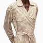 A person wears the 3.1 Phillip Lim Stripe Poplin Asymmetrical Wrap Shirt Dress, featuring beige and white stripes, a collar, chest pockets, a tied waist belt, and an asymmetrical handkerchief hem.