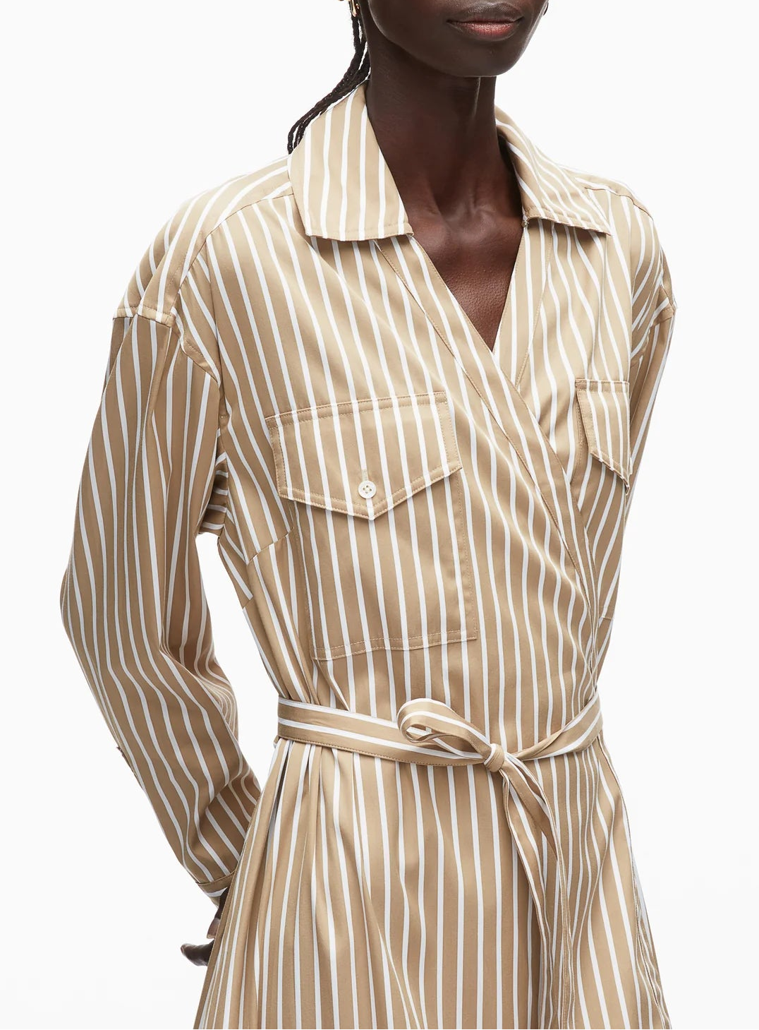 A person wears the 3.1 Phillip Lim Stripe Poplin Asymmetrical Wrap Shirt Dress, featuring beige and white stripes, a collar, chest pockets, a tied waist belt, and an asymmetrical handkerchief hem.