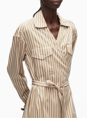 A person wears the 3.1 Phillip Lim Stripe Poplin Asymmetrical Wrap Shirt Dress, featuring beige and white stripes, a collar, chest pockets, a tied waist belt, and an asymmetrical handkerchief hem.