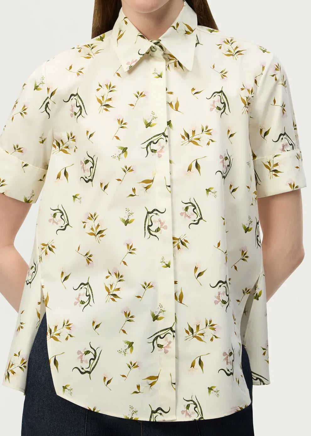 A person wearing the Adam Lippes Charlie Top—a short-sleeved, cream-colored blouse with a collared silhouette and floral and animal print—stands against a plain background.