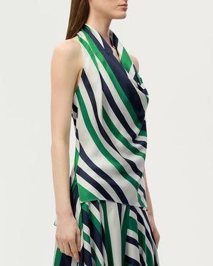 A woman wearing the Adam Lippes Cusette Printed Silk Twill Top—sleeveless, with green, navy, and white diagonal stripes—crafted from luxurious Italian silk twill and paired with a coordinating skirt.