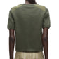 A person is seen from behind wearing the 3.1 Phillip Lim Merino Surplus Combo Top in olive green paired with a beige skirt featuring white stripes.