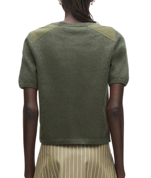 A person is seen from behind wearing the 3.1 Phillip Lim Merino Surplus Combo Top in olive green paired with a beige skirt featuring white stripes.