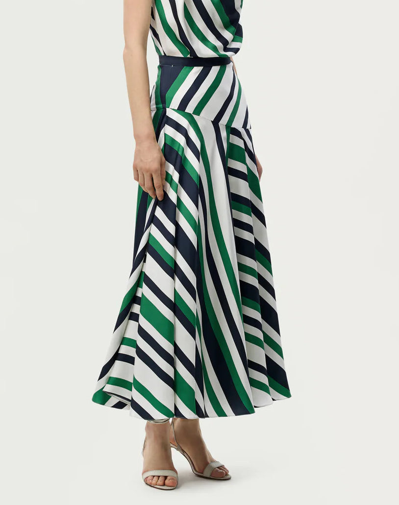 A person wearing a sleeveless top and the Adam Lippes Thea Printed Silk Twill Skirt, an Italian silk skirt with green, white, and navy diagonal stripes in a flared silhouette, paired with beige heeled sandals.