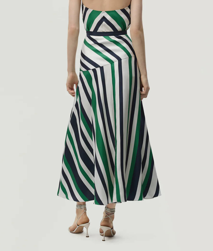 A person wearing the Adam Lippes Thea Printed Silk Twill Skirt, featuring diagonal green, black, and white stripes, stands facing away to highlight its flared silhouette and dynamic pattern—evoking the elegance of Italian silk.