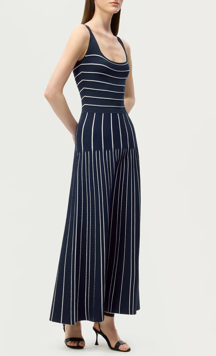 A woman stands against a plain background in the Gemma Compact Jacquard Dress by Adam Lippes, styled with black heeled sandals for an effortlessly chic look reminiscent of a navy jumpsuit.