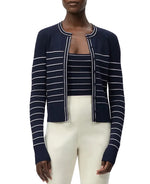 A woman wearing the Adam Lippes Faye Cardigan with self-covered buttons, layered over a matching striped top and paired with high-waisted cream pants.