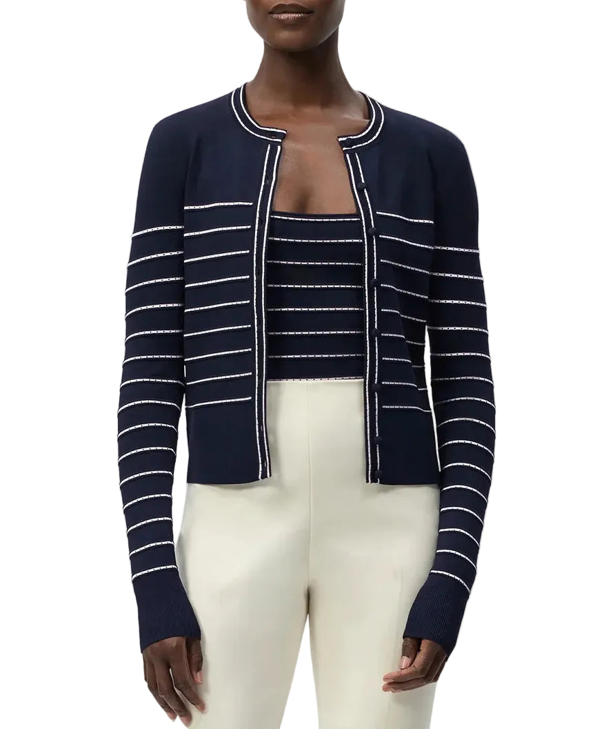 A woman wearing the Adam Lippes Faye Cardigan with self-covered buttons, layered over a matching striped top and paired with high-waisted cream pants.