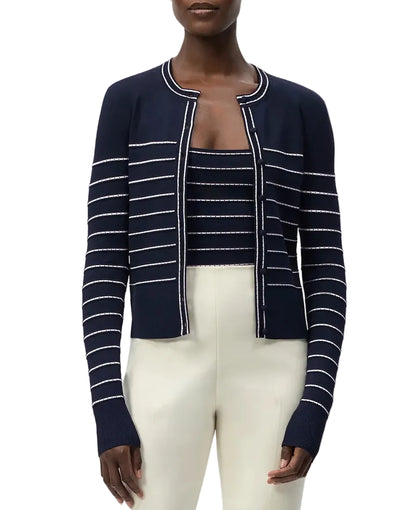 A woman wearing the Adam Lippes Faye Cardigan with self-covered buttons, layered over a matching striped top and paired with high-waisted cream pants.