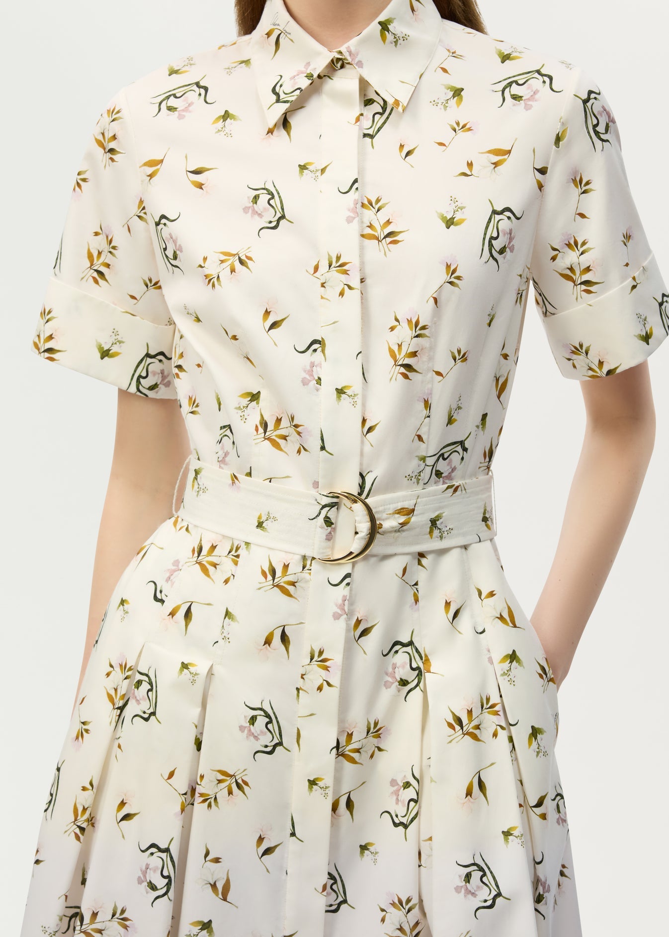 A woman wears the Leighton Dress by Adam Lippes, a short-sleeve, belted, collared button-up crafted from Italian cotton poplin with a playful dinosaur and leaf print on a light background.