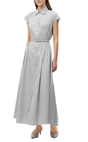 A woman wears the Adam Lippes Palmer Stripe Shirting Dress, a sleeveless, ankle-length design in white and ink stripes, crafted from Italian cotton shirting and featuring a collar, belt, and long fluid silhouette. She pairs it with grey heels.