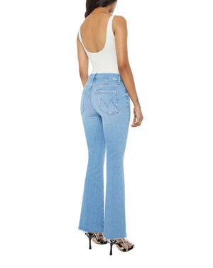 A woman in a white sleeveless bodysuit and Mother’s PETITES Lil Weekender Fray jeans—light blue, high-waisted, with flared legs—stands in high-heeled sandals, seen from the back.