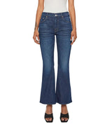 A person stands against a white background, hands relaxed by their sides, wearing the Lil’ Weekender mid rise dark blue denim flare jeans by Mother, styled with a white top and black open-toe heels.