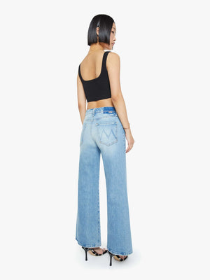 A woman stands with her back to the camera in a black crop top, black heels, and Mother’s PETITES The Lil Tomcat Roller Skimp high-waisted light blue wide-leg jeans against a plain white background.
