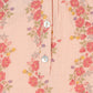Close-up of Konges Slojd's Baby Girls' and Girls' Coco Blouse, a peach-hued muslin top with a floral print in red, pink, yellow, and purple and three white center buttons.