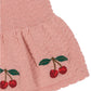Close-up of Konges Slojd's Baby Girls' and Girls' Cypres Cardigan, a pink knitted cotton piece with a peplum silhouette, ruffled edge, and embroidered red cherries with green leaves.