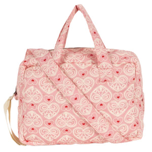 The Konges Slojd Lacy Pink Doll Bag features red hearts and floral patterns, soft shoulder straps, and a handy grab-and-go handle for easy carrying.