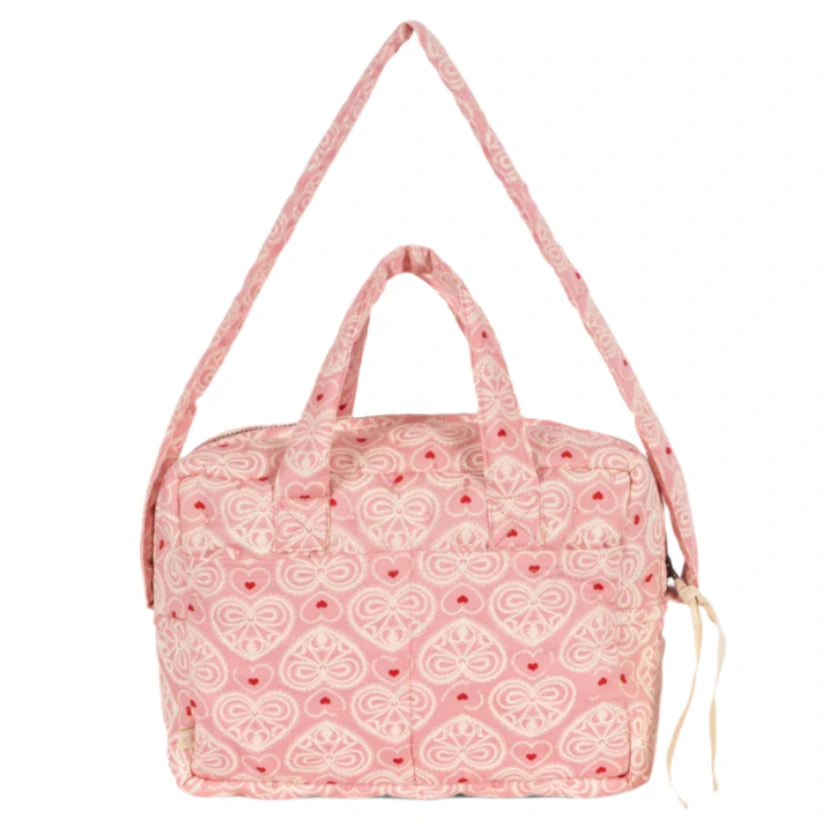 The Konges Slojd Lacy Pink Doll Bag is a quilted pink carryall with soft straps, grab handle, heart pattern, and front pocket—perfect for stylish doll outings.