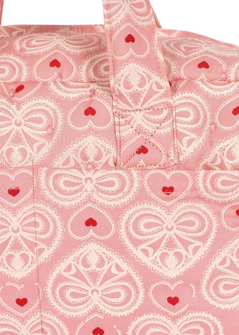 The Konges Slojd Lacy Pink Doll Bag features a pink fabric with white lace-like heart designs, small red hearts, soft shoulder straps, and two handles for easy carrying.