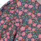 Close-up of the Konges Slojd Girls' Cianna Blouse—a woven cotton top with puffed shoulders, set against a dark background and adorned with a colorful floral print in pink, green, orange, and beige.
