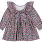 The Konges Slojd Girls' Cianna Bow Dress is a long-sleeve organic cotton dress featuring a ruffled collar, chest bow, and pink floral pattern on a dark background.
