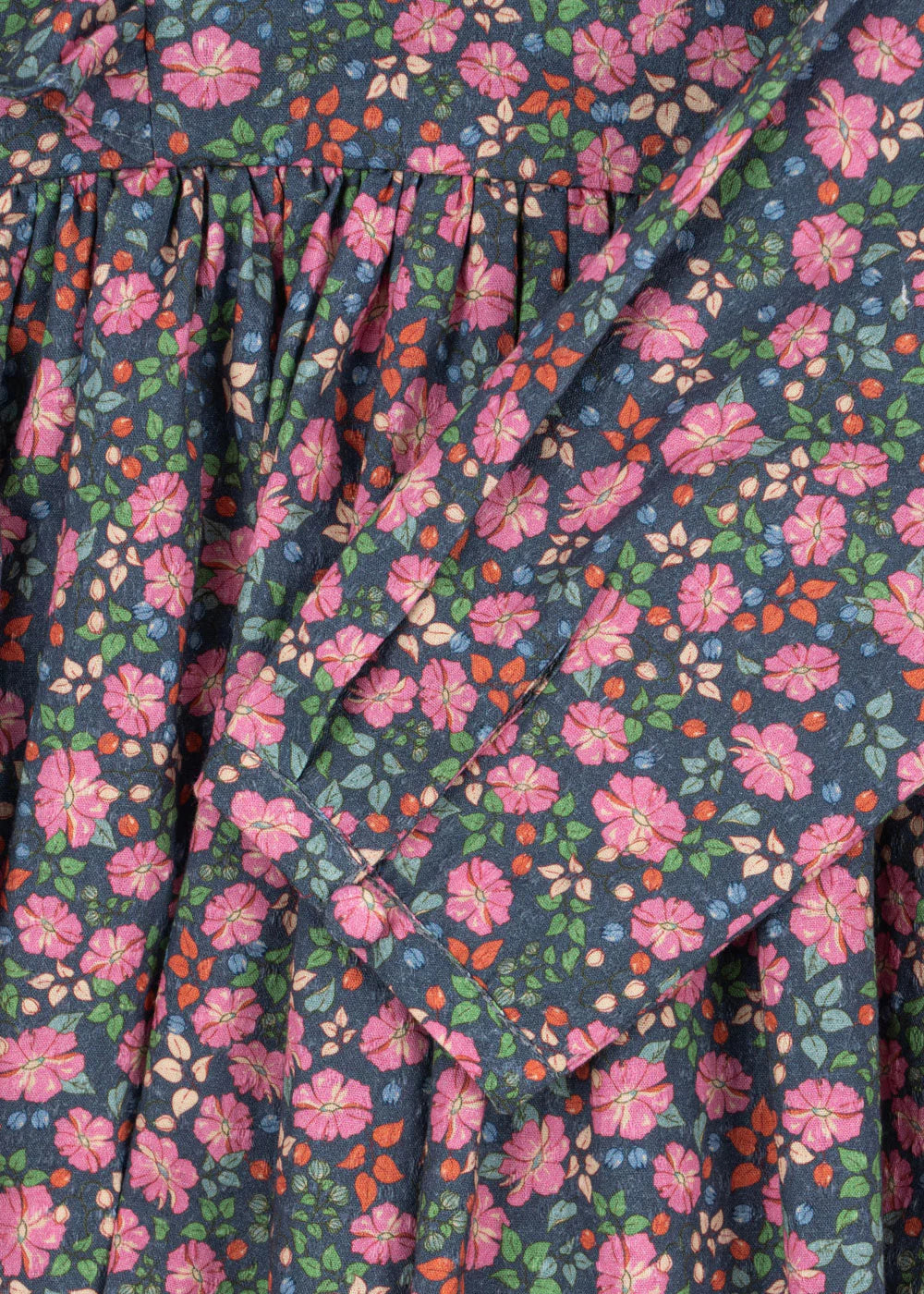 Close-up of the Konges Slojd Girls' Cianna Bow Dress, made from organic cotton with a colorful floral pattern—pink, red, orange, and green flowers on dark fabric—featuring gathered and folded details.