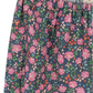 A close-up of the Girls' Cianna Pants by Konges Slojd, featuring a blue background with pink, orange, and green floral patterns. The gathered elastic waist ensures comfort, and a partially visible interior label is shown.