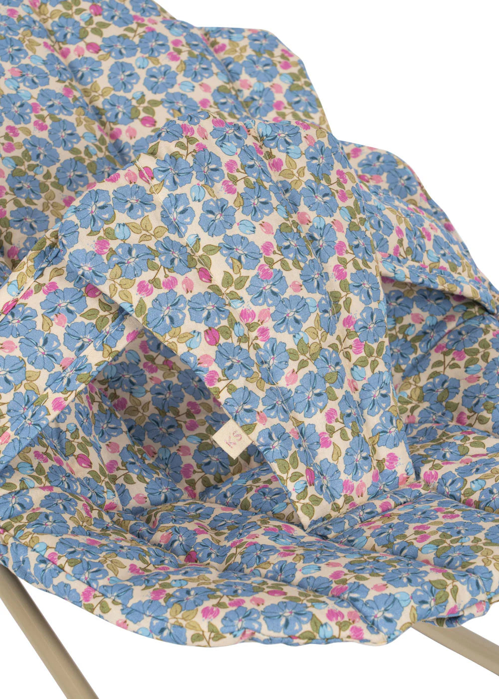 Close-up of a washable cotton cushion with blue, pink, and green floral pattern on white, placed on a metal-framed Konges Slojd Doll Bouncer—ideal for your child's playtime.