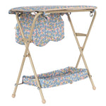 The Konges Slojd Doll Changing Table features a beige metal frame, floral-patterned cover, storage pockets, and a lower shelf for convenience.