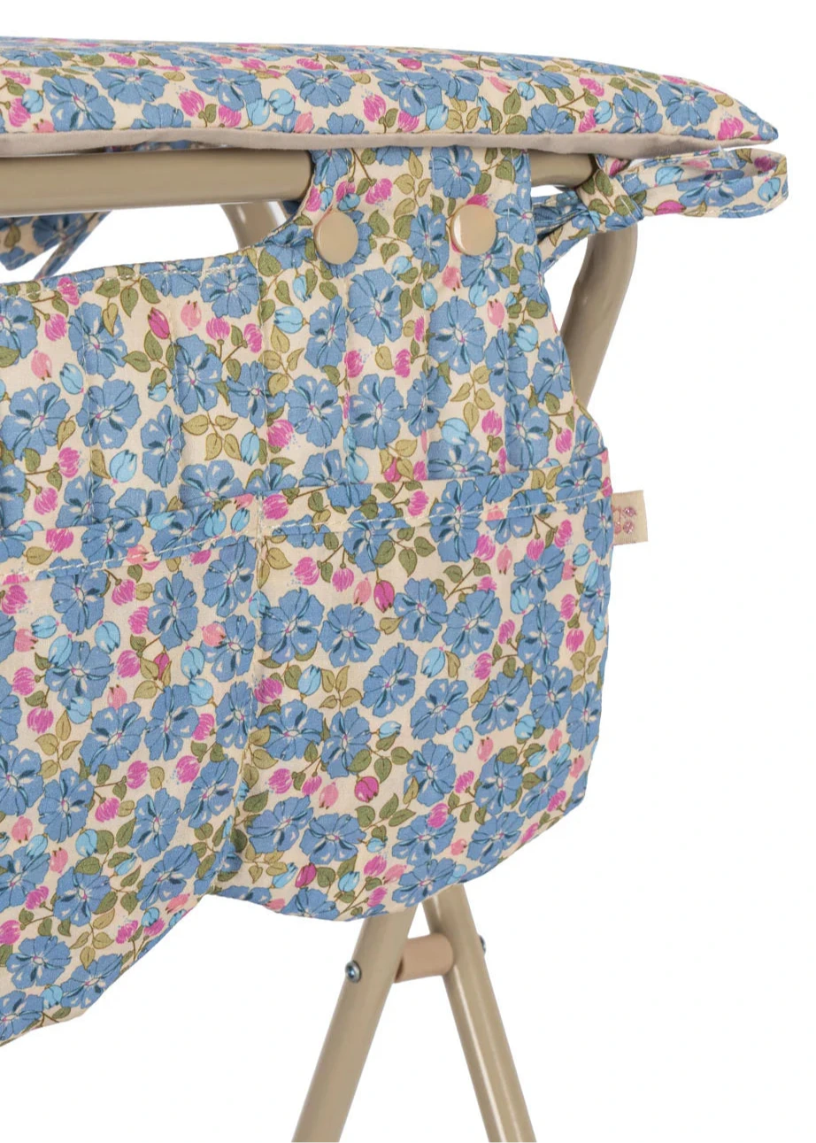 Close-up of the Konges Slojd Doll Changing Table featuring a padded cover with a blue, pink, and green floral pattern on a beige metal frame.