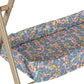 A close-up of the Konges Slojd Doll Changing Table, featuring a beige metal frame, floral-patterned cushion with blue, pink, and green flowers, and convenient storage pockets on the side.
