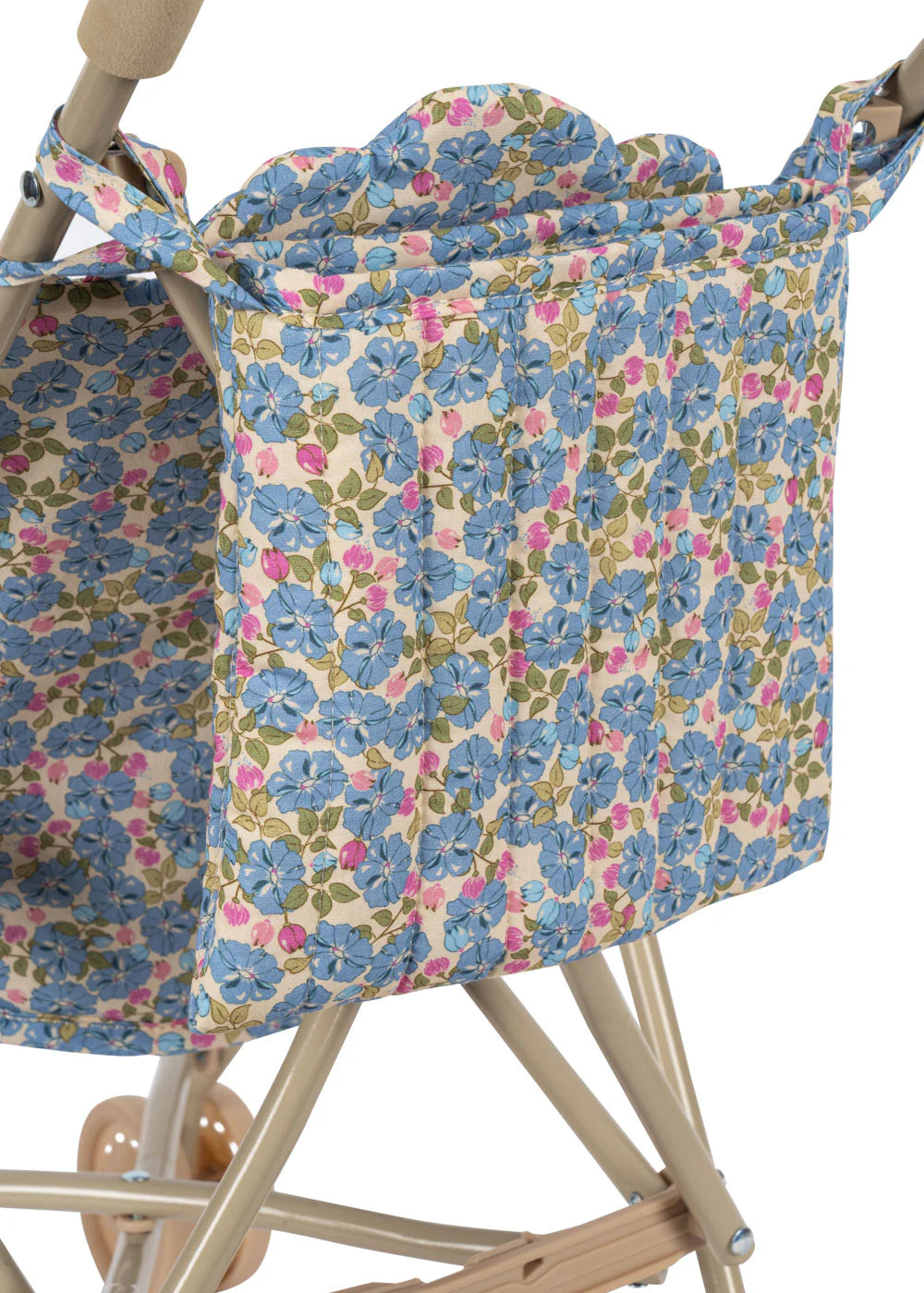 A close-up of the Konges Slojd Doll Stroller shows its blue, pink, and green floral fabric storage pocket, with a beige frame and double wheels partly visible.