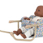 The Konges Slojd Doll Table Chair seats a baby doll in a white outfit, surrounded by a floral print and supported by an iron frame with quilted cotton padding for comfort.